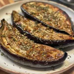 Close-up view of cooked aubergine slices, golden brown and crispy from an air fryer.