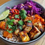 A colorful Buddha bowl featuring halloumi cheese, sweet potatoes, red cabbage, and garnished with coriander.
