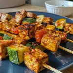 ['Close-up view of colorful vegetarian vegetable sticks with tofu on a plate.', 'Side perspective of freshly prepared vegetable sticks made from zucchini, carrots, and peppers with tofu.', 'Juicy vegetarian dish featuring assorted vegetable sticks and tofu next to a dipping sauce.', 'Vibrant arrangement of grilled vegetable sticks with tofu, highlighting their textures and colors.']