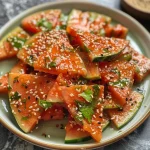 Close-up of crispy watermelon rind snacks, garnished with sesame seeds and green chilies.