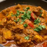 A close-up view of a bowl of chicken pumpkin curry, featuring vibrant colors and rich textures.
