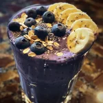 Close-up side view of a creamy blueberry smoothie in a glass, topped with fresh blueberries.