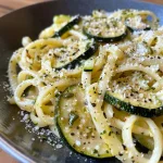 Close-up view of high protein pasta with zucchini and lemon, garnished with basil.